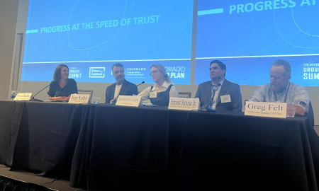 The four panelists from the Progress at the Speed of Trust Panel sit at a long table in the front of the room