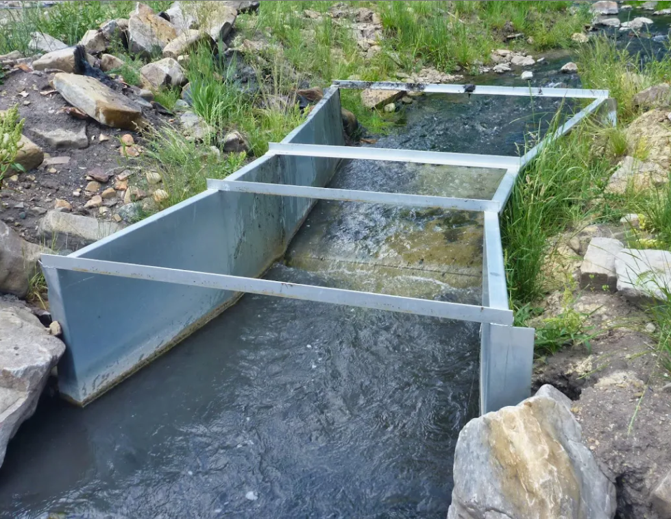 A metal flume diverts water into an irrigation ditch.
