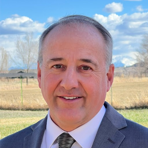 Jason in a blue suit standing near a grass field.