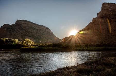 Photo of Colorado River at the base of two mesas with the setting sun in the background