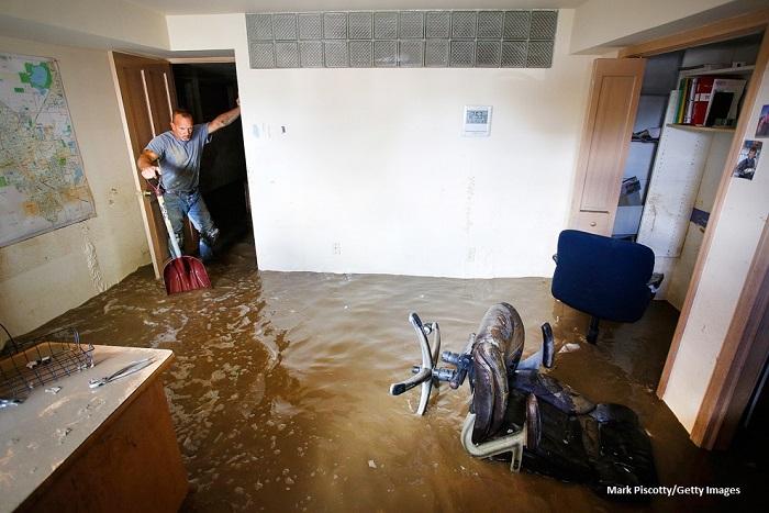 A man with a shovel looking at the brown floodwaters in a house during the 2013 South Platte Flood