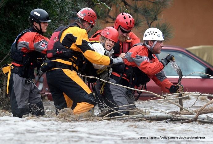 Four men in safety gear helping a woman through flood water in 2013