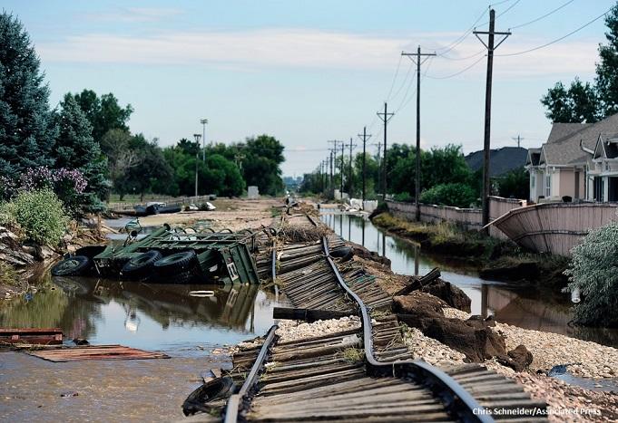 Ruined railroad tracks run along a flooded ditch and an overturned 6-wheeled truck after the 2013 South Platte flood